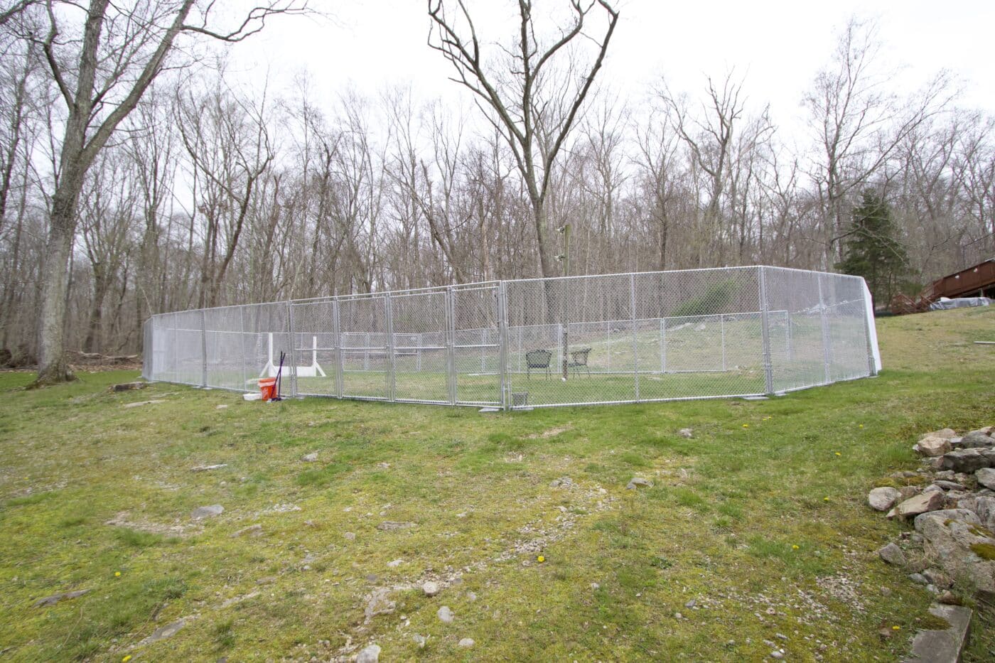 outdoor chain link kennel fencing with two black chairs and a white jump for dogs